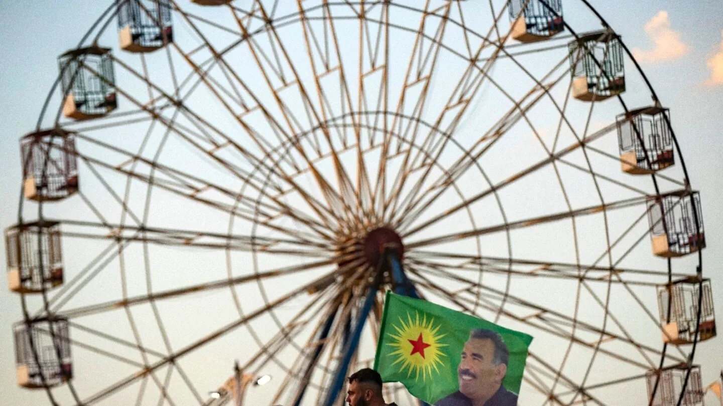 رجل يحمل علمًا عليه صورة عبد الله أوجلان أمام عجلة فيريس.