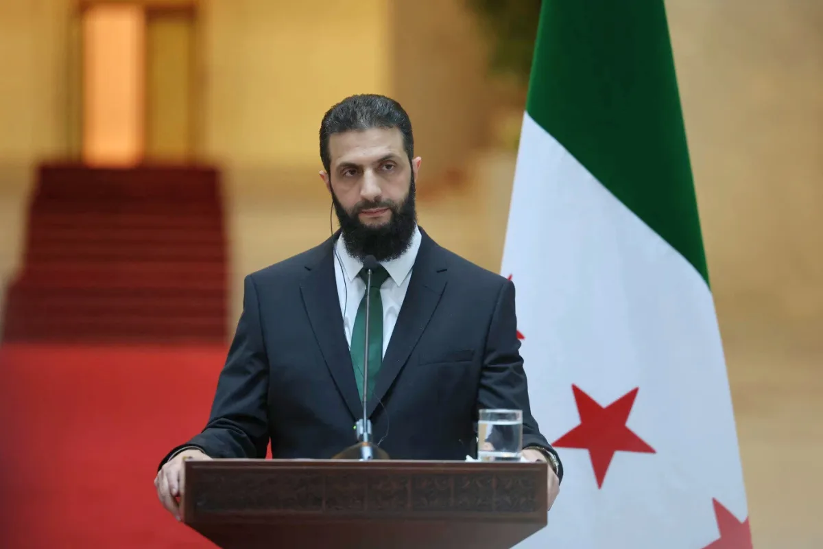 الرئيس السوري أحمد الشرع في مؤتمر دولي مع علم سوريا