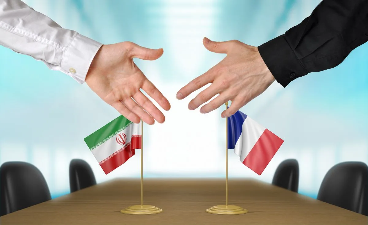يدان تمتدان للمصافحة أمام علمي إيران وفرنسا على طاولة مؤتمر
