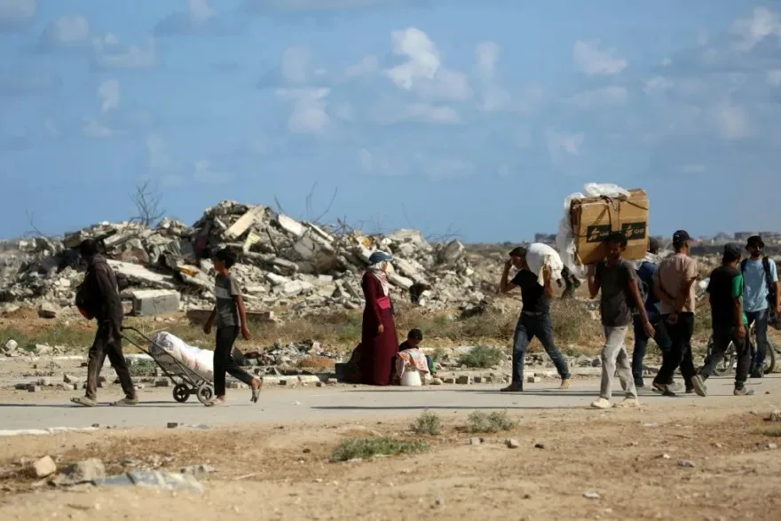 نازحون فلسطينيون يحملون متعلقاتهم ويسيرون وسط أنقاض المباني المدمرة في قطاع غزة