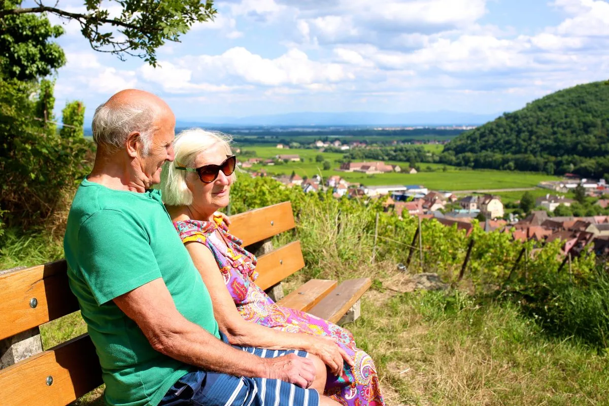 زوجان من كبار السن يستمتعان بالمنظر الطبيعي الجميل من مقعد خشبي في أوروبا