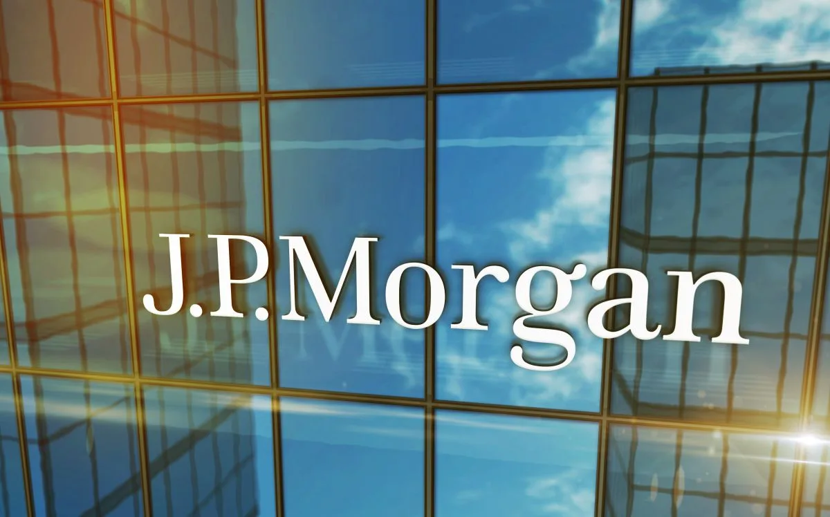 شعار بنك جي بي مورغان على واجهة مكتب زجاجية مع إطلالة على السماء الزرقاء والغيوم