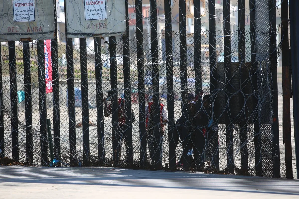 مهاجرون خلف سياج حدودي مزود بأسلاك شائكة عند الحدود الأمريكية