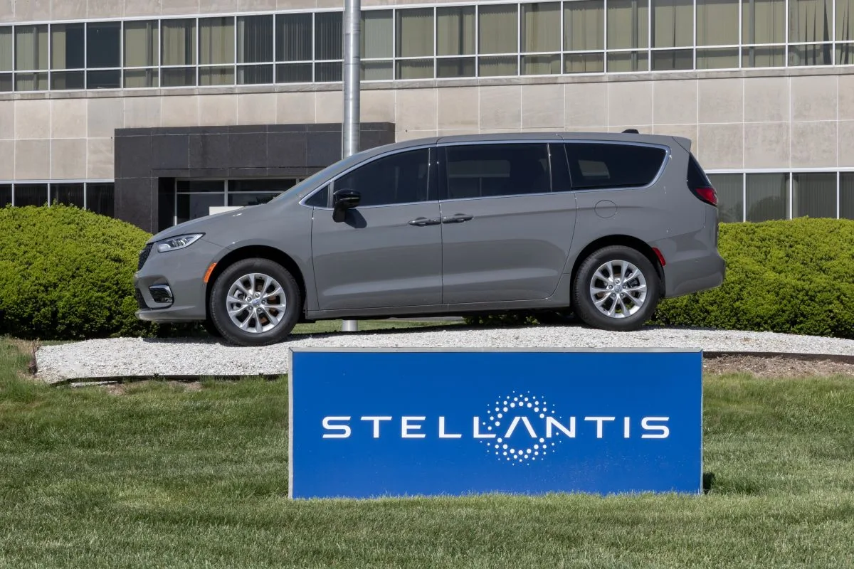 سيارة رحلات رمادية من إنتاج شركة ستيلانتيس موقوفة أمام لافتة زرقاء برسم لوغو الشركة