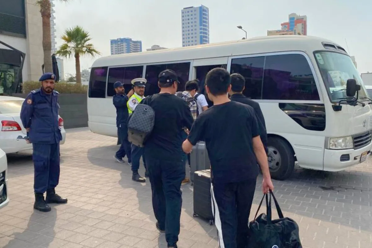 رجال أمن يرافقون أشخاصًا يرتدون ملابس مدنية باتجاه حافلة صغيرة بيضاء