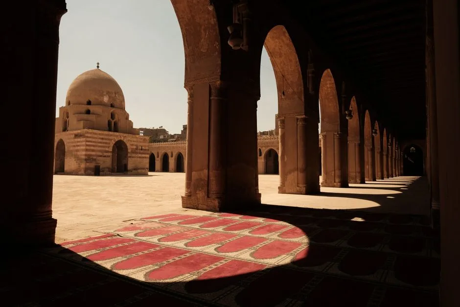 View of Ibn Tulun Mosque's courtyard with arches and carpet under sunlight in Cairo, Egypt.